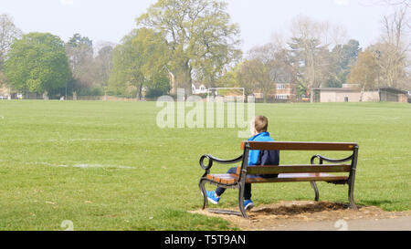 teen boy sitting on bench in empty british park dressed in training kit. Stock Photo