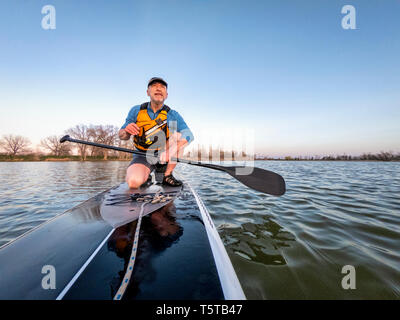 athletic senior man on a stand up paddleboard enjoing sunset lover a calm lake in Colorado, bow view Stock Photo