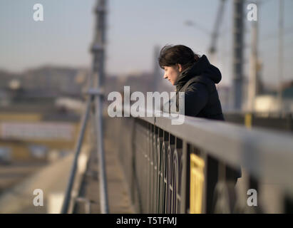 Lonely young brunette girl stands on the bridge on a sunny day Stock Photo