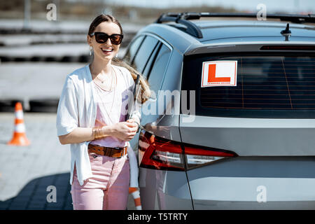 Portrait of a young female student standing near the learning car on the training ground at the drivers school Stock Photo