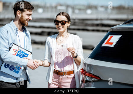 Instructor shaking hands with happy woman getting a driver's license while standing together on the training ground outdoors Stock Photo