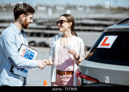 Instructor shaking hands with happy woman getting a driver's license while standing together on the training ground outdoors Stock Photo