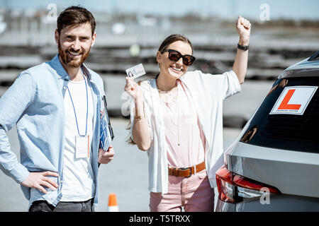 Instructor with happy woman getting a driver's license while standing together on the training ground outdoors Stock Photo
