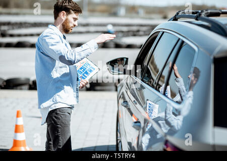 Instructor explaining the route scheme of training for a driver who sits in the learning car on the training ground Stock Photo