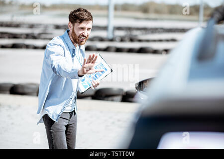Male instructor showing stop with hands while teaching to park a car on the training ground at the school Stock Photo