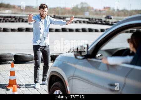 Male instructor showing stop with hands while teaching to park a car on the training ground at the school Stock Photo