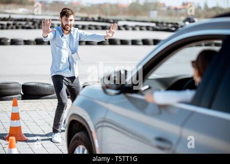 Male instructor showing stop with hands while teaching to park a car on the training ground at the school Stock Photo