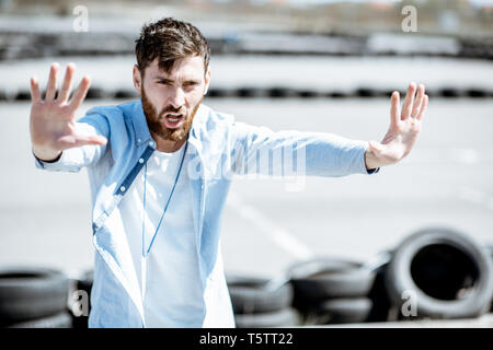 Male instructor showing stop with hands while teaching to park a car on the training ground at the school Stock Photo