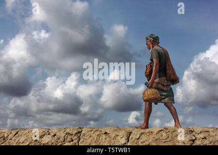 A fisherman walks home along the banks of the Rupsha River in Khulna, Bangladesh, after a day spent catching fish. Stock Photo