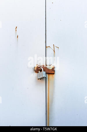 Locked simple metal padlock hanging on rusted hasp on plain metal doors of garden shed. Stock Photo