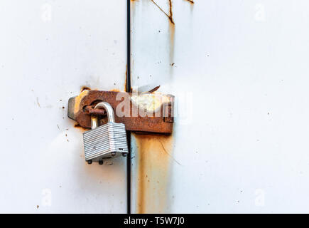 Locked simple metal padlock hanging on rusted hasp on plain metal doors of garden shed. Stock Photo