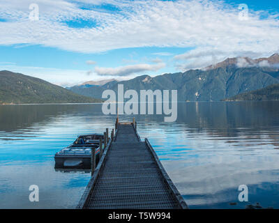 Jet boat at wharf, clouds and blue sky reflected in calm water, distant hills, Lake Hauroko, Fiordland National Park, Southland, New Zealand Stock Photo