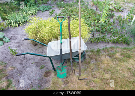 A garden tool and a wheelbarrow used on a personal plot. An old shovel, a pitchfork and a hoe against the backdrop of a wheelbarrow. Home garden and a Stock Photo