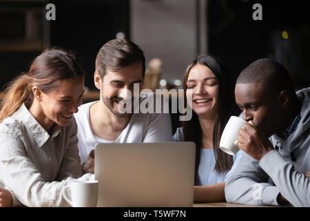 Diverse cheerful friends sitting in cafe watching video on computer Stock Photo