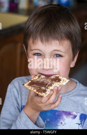 A closeup portrait of a cute blue-eyed child eating a matzoh cracker with chocolate spread. Stock Photo