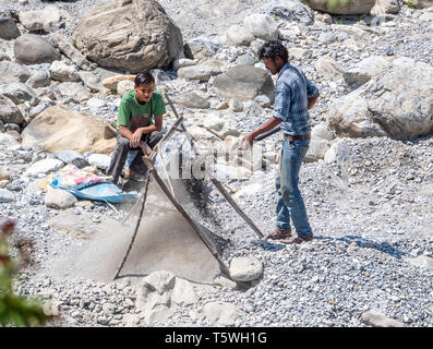 Young men sieving sand  for building from river gravel on the Saryu river near Bageshwar in Uttarakhand Northern India Stock Photo