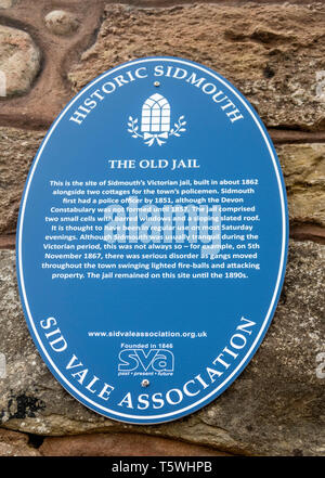 Blue plaque sign telling about the old barred windows of Sidmouth Jail left in a wall as part of a new housing development. Town jail bars. Stock Photo