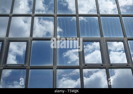 Blue sky and white clouds reflected on dirty windows. Office building facade closeup abstract background. Stock Photo