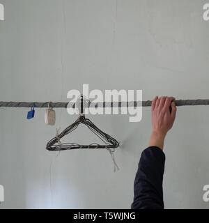 Hand on rusty clothesline with old wire hangers and moth repellent in abandoned interior. Stock Photo