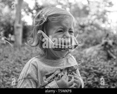 Little girl crying in the garden on spring background. Sad and angry concept. Stock Photo