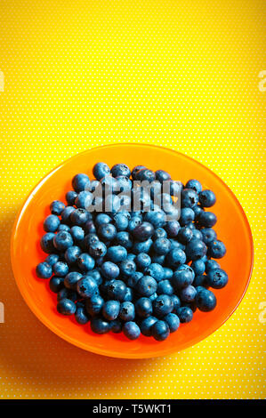 orange bowl filled with blueberries on a yellow background Stock Photo