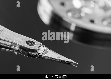 Macro black & white image of the actuator arm and read / write head reading and writing data from and to a computer hard disk drive (HDD) platter. B&W Stock Photo