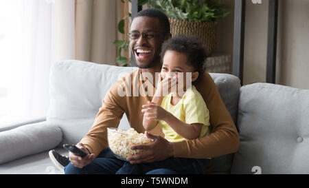 African father holding on lap little son family watching movie Stock Photo