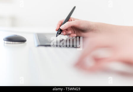 Close up side view of female holding digital pen and using graphic tablet at the desk. Stock Photo