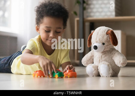 Adorable african kid lying on warm floor play with toys Stock Photo