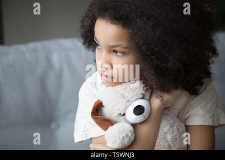 Unfortunate stray biracial kid girl embrace stuffed toy looking aside Stock Photo