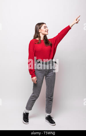 Young woman wearing red sweater miling and looking at the camera pointing with hand and fingers to the side. Stock Photo