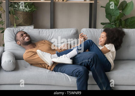 Laughing funny father play with daughter lying on sofa Stock Photo