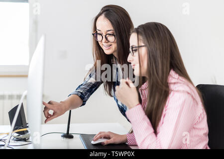 Two cheerful fashionable females looking and showing something on computer screen at the office. Stock Photo