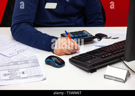 Young male administrator talking on the phone at work, holding the phone to his ear and at the same time making notes on the paper with a pen sitting  Stock Photo