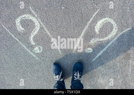 Female standing in front of two roads, unable to make the right decision concept with question marks above his head Stock Photo