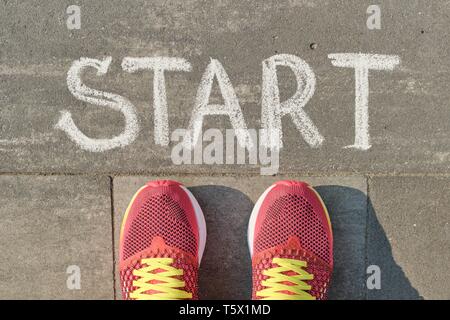 Word start written on gray pavement with woman legs in sneakers, view from above. Stock Photo