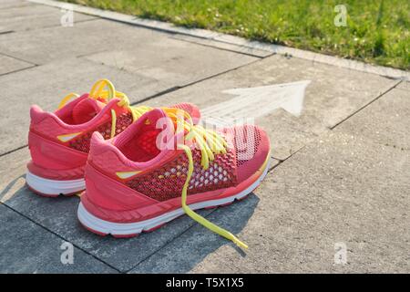 Sneakers with the arrow sign painted on gray sidewalk, top view. Stock Photo
