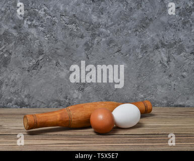 The cooking process. Rolling pin, eggs on a wooden shelf on a concrete wall Stock Photo