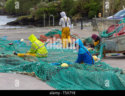 fishermen mending or repairing fishing nets on the jetty quayside Stock Photo
