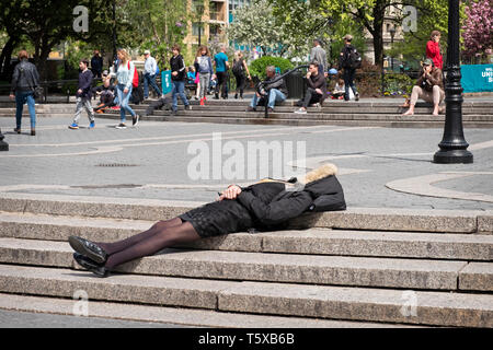 An anonymous well dressed woman in an overcoat sleeping on the steps on Union Square Park in Lower Manhattan, New York City. Stock Photo