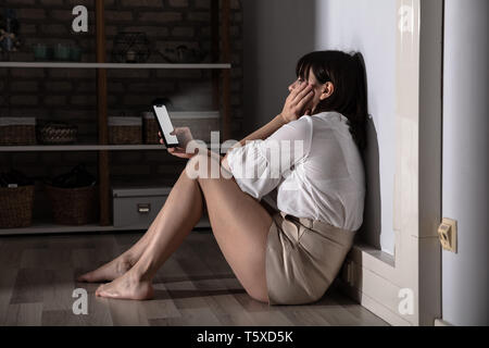 Sad Woman Checking Smartphone Sitting On Floor In Living Room Stock Photo