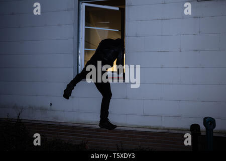 Rear View Of A Burglar Entering In A House Through A Window Stock Photo