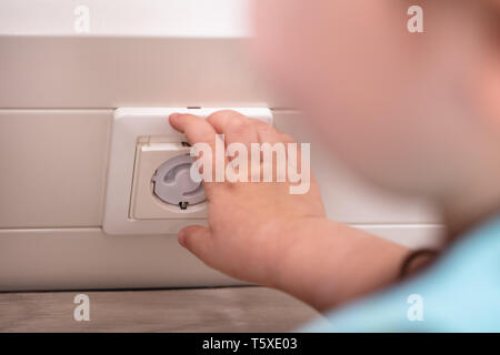 Baby Girl Playing With Electrical Extension On Floor At Home Stock Photo