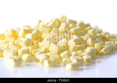 Pastel yellow mini marshmallows scattered on a white reflective surface. Stock Photo