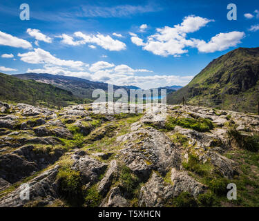 Majestic view on scenic mountain valley in Snowdonia, North Wales, UK, in springtime.Rocky hill in foreground, mountain, lake and blue sky with clouds. Stock Photo