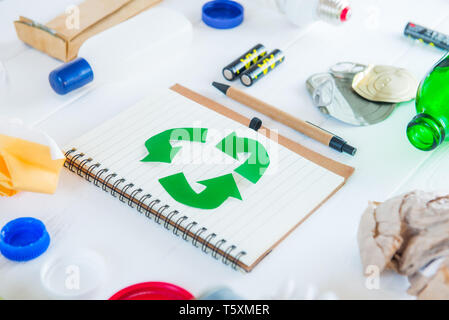 Recycle paper notebook with Green eco symbol surrounded with non recycling garbage and reusable waste as metal, plastic, old paper, glass products on  Stock Photo