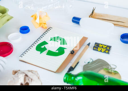 Recycle paper notebook with Green eco symbol surrounded with non recycling garbage and reusable waste as metal, plastic, old paper, glass products on  Stock Photo