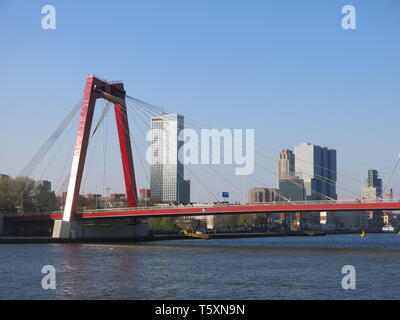 Taken from midway across the Nieuwe Maas, a view of the bright red Willemsbrug bridge and the city of Rotterdam in the background Stock Photo