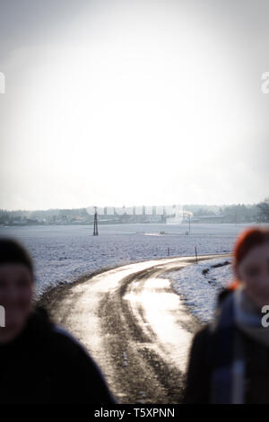 two young pretty woman walking and laughing on a rural path on a sunny snowy winter sunday Stock Photo