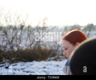 young pretty ginger girl walking on a rural path on a cold sunny snowy winter sunday Stock Photo